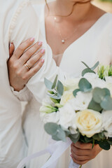 The bride in a white dress embraces the hand of the groom in a white shirt with her hand, wearing a...