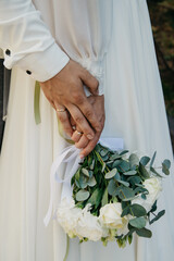 The bride in a white dress holds a bouquet of white roses in her hand and on her hand lies the...