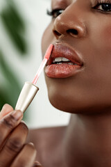 Woman applying lip gloss in a beauty routine at home during the day with plants in the background
