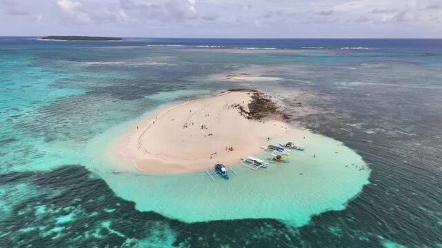 Aerial drone orbit of Naked- originally Pansukian Island, Siargao Islands, Philippines, showing white sandbar, tourists, clear turquoise water, and traditional outrigger boats in the tropical waters