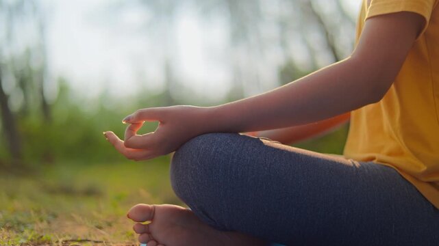 Close up shot of a serene women sitting in padmasana meditation pose during golden hour in the forest.