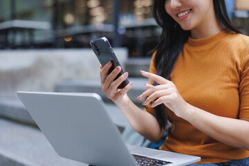 Smiling businesswoman using smartphone and laptop computer outdoors