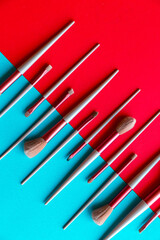Creative flat lay of a professional makeup brush set displayed symmetrically on a split red and turquoise background. The vibrant color block design emphasizes the contrast and makes the cosmetic