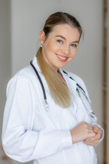 Smiling female doctor in white coat holding hands with a stethoscope