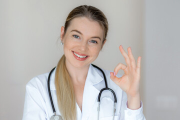 Smiling doctor with stethoscope making an okay hand sign in a bright setting