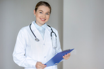 Confident female doctor holding clipboard and stethoscope in a hospital setting