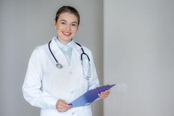 Smiling medical professional holding a clipboard wearing a white coat and stethoscope
