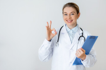 Smiling doctor making OK gesture and holding clipboard with confident expression