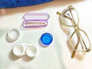 Contact lens care items are neatly arranged near eyeglasses on a clean surface
