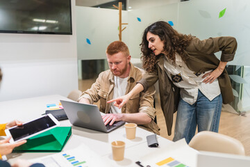 Businesswoman pointing at laptop screen while explaining something to her colleague during a...