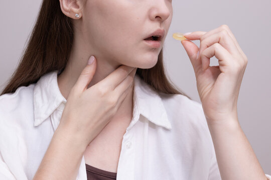 Woman holding throat and preparing to take lozenge for sore throat relief. Concept of cold treatment, throat pain, and seasonal illness.