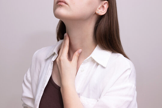 Close-up of woman touching throat area checking thyroid gland. Concept of thyroid screening, thyroid self-exam, endocrine health.