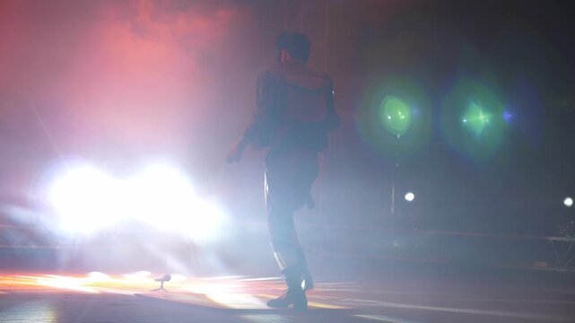 A clown with a funny hairstyle entertains guests in the circus arena in the light of colorful spotlights and smoke. He is tap dancing and twirling strings in his hands. Circus performance.