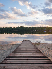 A wooden boardwalk leading to a small pier. Wooden walkway on the beach at sunset. 
