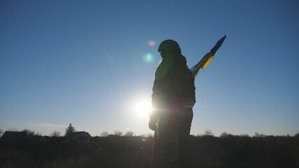 Female and male soldier of ukrainian army stands at the peak of hill waving blue-yellow banner. Young woman and man in military uniform lifted flag of Ukraine against blue sky with sun. Slow motion