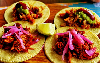 Quatre tacos garnis sur une planche de bois avec un quartier de citron.