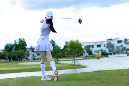 Asian woman happy and fun while playing golf on the golf course. Golfer hitting golf shot with driver club on course. Beautiful woman smiling and holding a golf club while standing on green lawn.