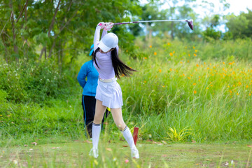 Asian woman happy and fun while playing golf on the golf course. Golfer hitting golf shot with...