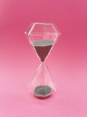 Glass hourglass with gray sand on pink background, symbol of time and deadline in clean minimalistic composition