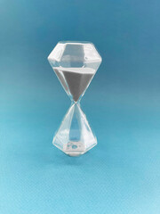 Transparent hourglass with gray sand on blue background, concept of time, patience and deadline in minimal style