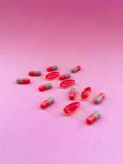 Pink and grey capsules and red softgel pills on pink background, medical supplements or pharmaceutical concept for health and treatment