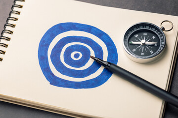 Notebook with hand-drawn target, black marker, and compass on desk, symbolizing setting goals,...