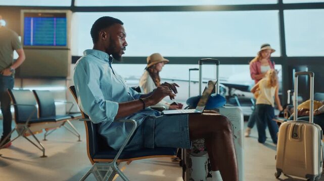 A person at the airport waiting area is checking a tablet, with other travelers around and airplanes in the background.