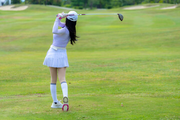 Asian woman happy and fun while playing golf on the golf course. Golfer hitting golf shot with...