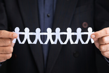 Close-up of businessman holding a paper chain of human figures, symbolizing teamwork, unity,...