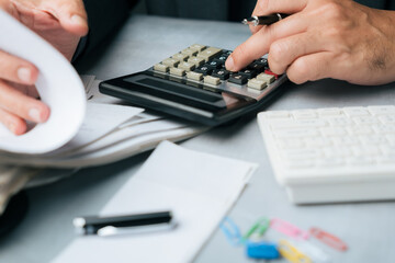 Close-up of a hand using a calculator to recalculate bill amounts, with documents, pen, and paper clips on the desk, representing financial accuracy and expense management