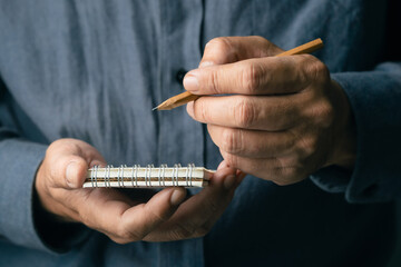 Close-up of a man writing important notes on a small spiral notebook using a pencil, symbolizing focus, idea capturing, and personal organization