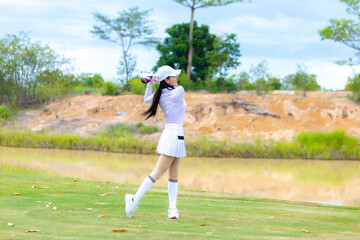 Asian woman happy and fun while playing golf on the golf course. Golfer hitting golf shot with...