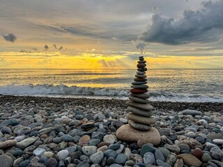  Balanced stones on pebble beach at sunset with ocean waves and dramatic sky