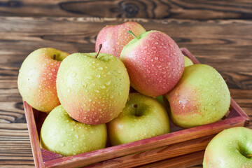 Fresh apples in a wooden box on a rustic wooden background.