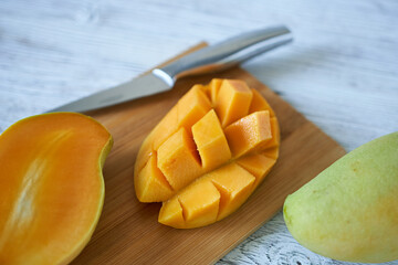 chopped mango on a wooden board with a knife on a white table
