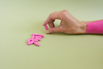Female hand holding pink pills on green background. Focus on hand.