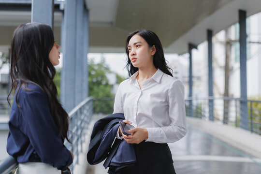 Two businesswomen talking seriously on a walkway in a modern office building
