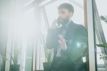 Businessman dressed in formal attire talking on his phone, with bright natural light and lens flare...