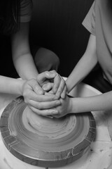 Mother and son making pottery on wheel at ceramics studio with hands covered in clay