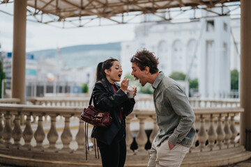 Two young adults sharing a lighthearted moment while enjoying a dessert outdoors in a lively urban...