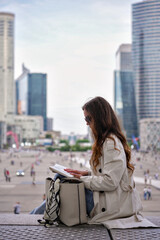 Fototapeta premium A woman reads a book while sitting in La Defense Paris with skyscrapers and urban life in the background 