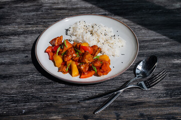 Pork in sweet and sour sauce with boiled rice on a plate. 