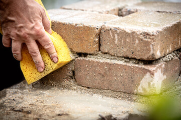 a man washes the freshly laid bricks of a post with a sponge