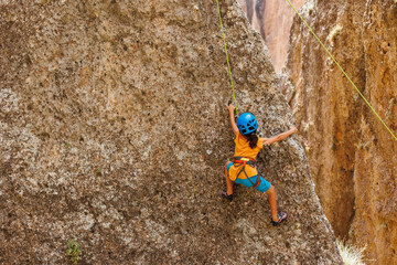 Obraz premium sport in summer camp. a child is rock climbing at a summer camp. rock climber boy. sport in nature. cute teenager climbs a rock with a belay.