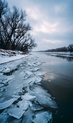 Frozen river scene with icy shores and stark trees against a dramatic winter sky reflecting calmness and winter's