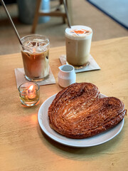 Cozy café setup with a heart-shaped palmier pastry and two iced coffee drinks on a wooden table, perfect for a relaxing coffee break.