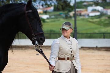 Young and beautiful woman holds and pulls the reins of a black purebred Spanish horse in Andalusia,...