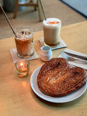 Cozy café setup with a heart-shaped palmier pastry and two iced coffee drinks on a wooden table, perfect for a relaxing coffee break.