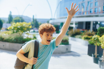Redheaded teen waves with excitement and energy in front of a modern school building