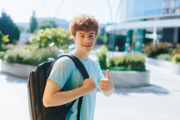 Smiling redheaded teen gives a thumbs-up outside school on a sunny afternoon